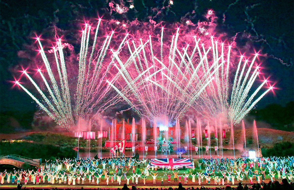 Photograph of Kynren castle with fireworks illuminated above the castle and the actors beneath with a Union Jack Flag sitting central to the photograph