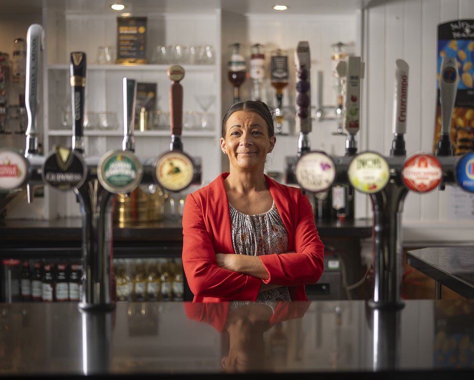 Land Lady stood behind bar with beer pumps in fore ground