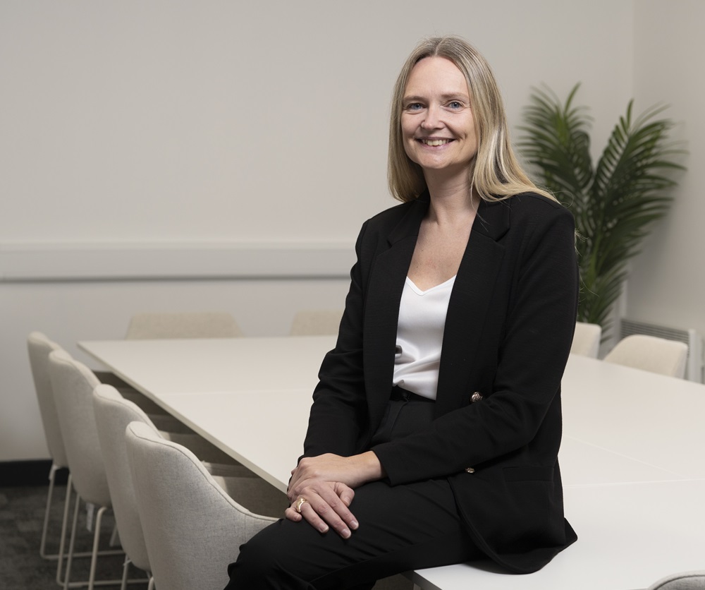Jennifer Phillips Head of Community and careers at the college sitting on edge of table looking into camera.