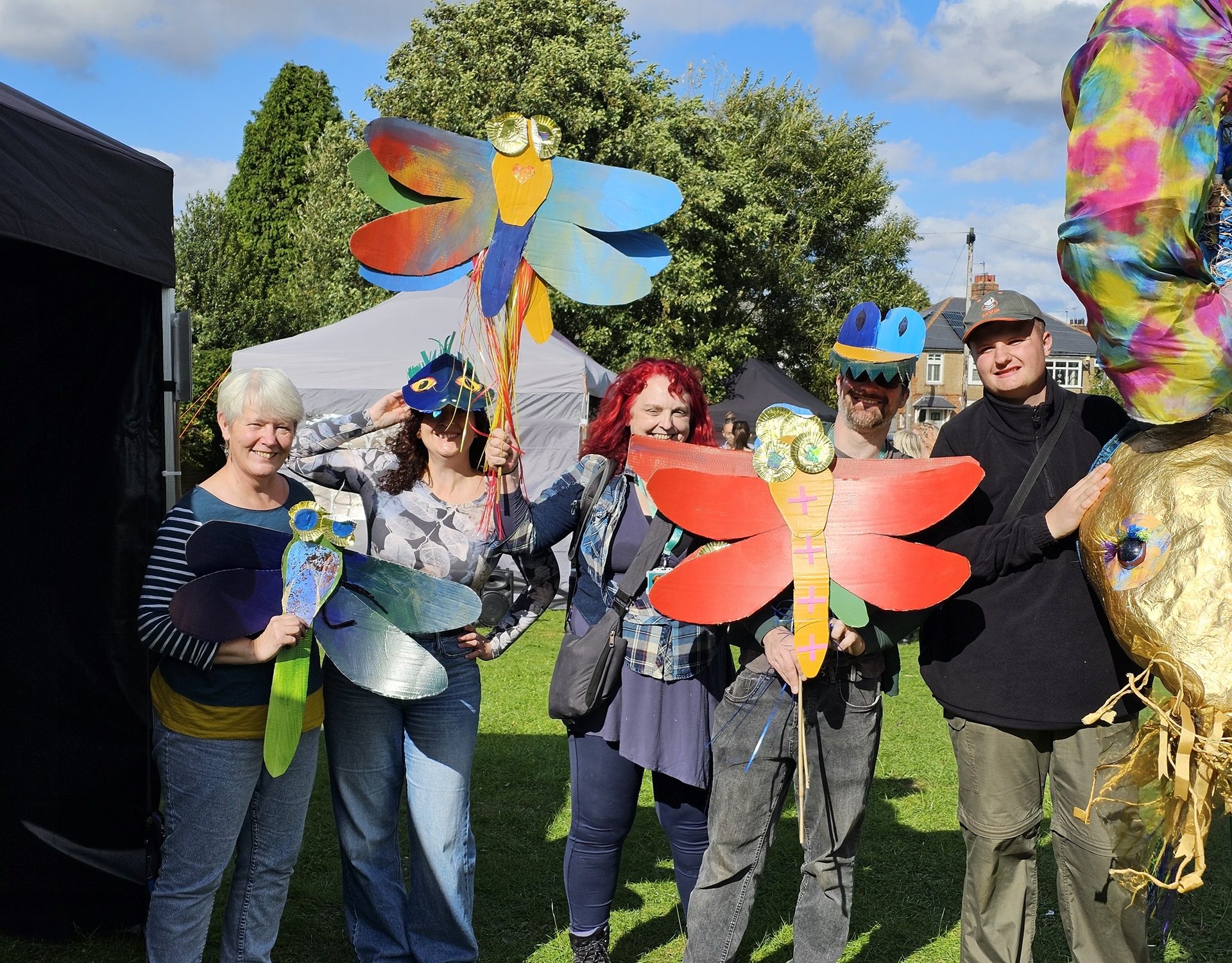 Group of people holding colourful artwork in the shape of dragonflies.