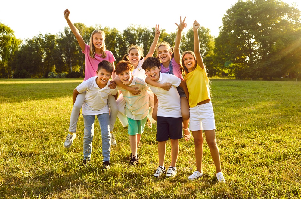 7 children in a field on a summers day with arms in the air.