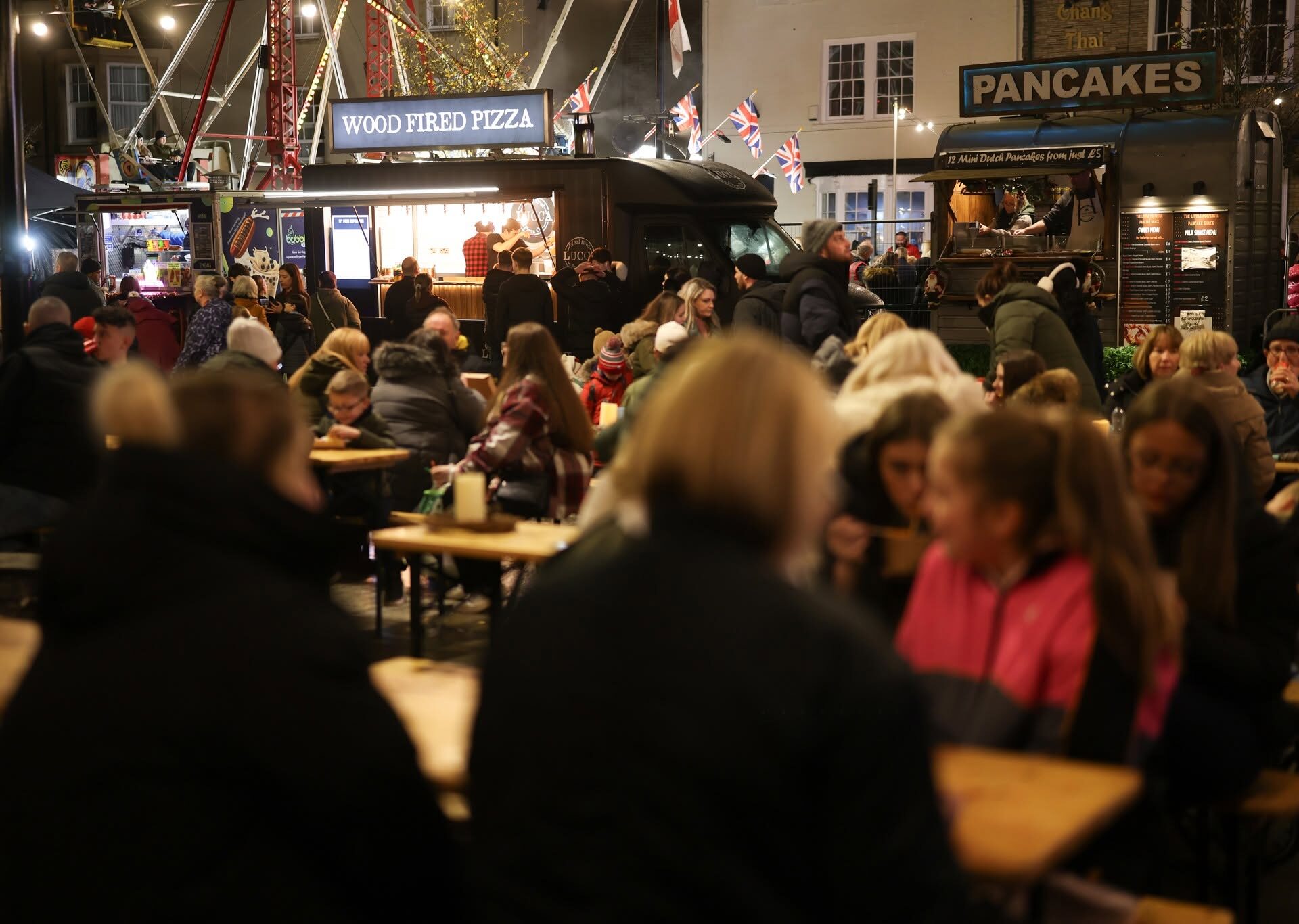 People sitting at tables in Bishop Auckland Market Place with a food stall in the background